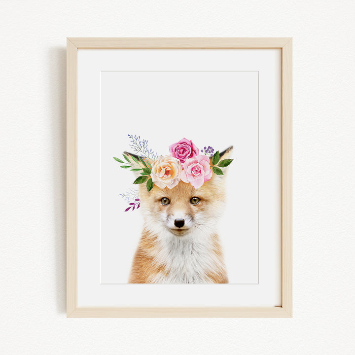 A framed print of a fox wearing a floral crown of pink and white roses and greenery.