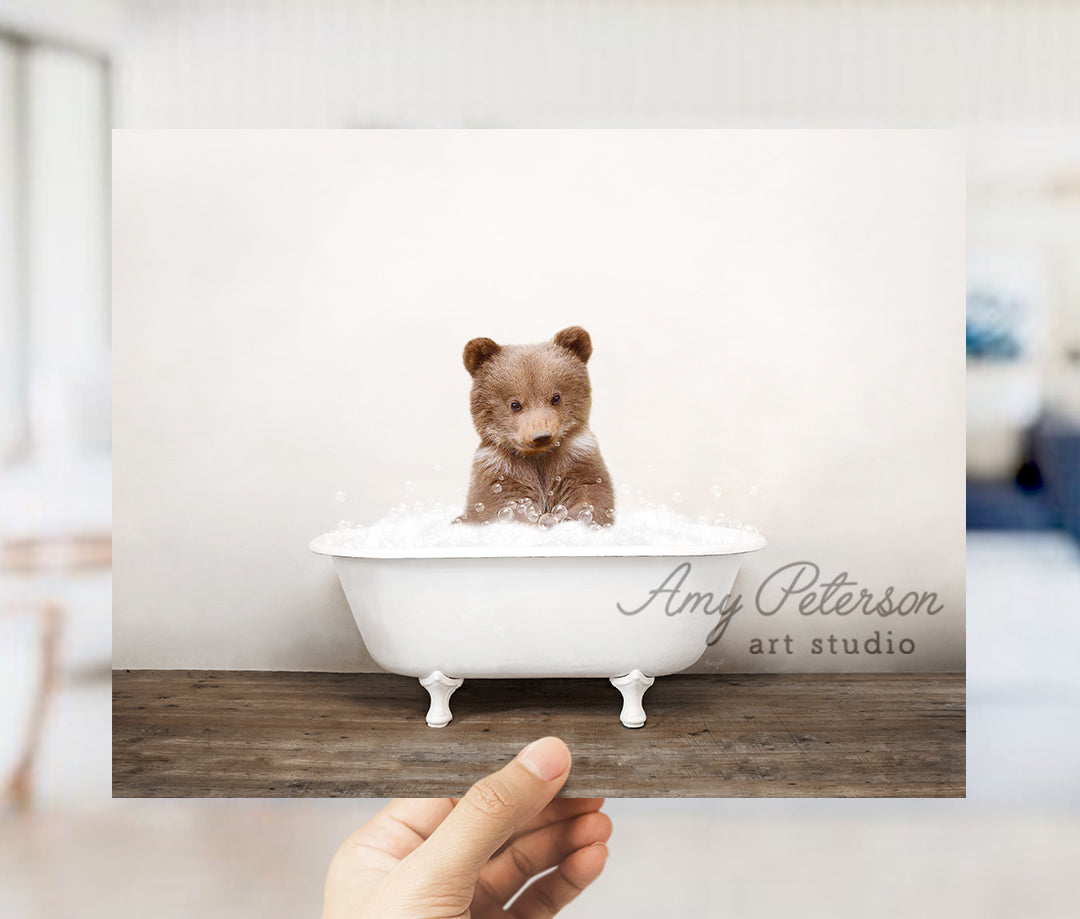 a hand holding up a photo of a teddy bear in a bathtub