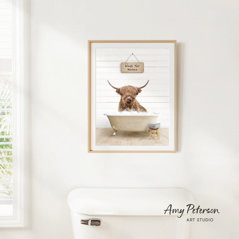 A framed image of a Highland cow sitting in a bathtub, with a sign above it that says "Wash Your Horns".