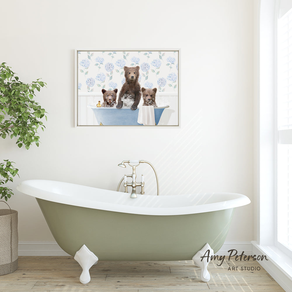 A framed image of three bears sitting in a bathtub is displayed on the wall above a green clawfoot bathtub in a bathroom.