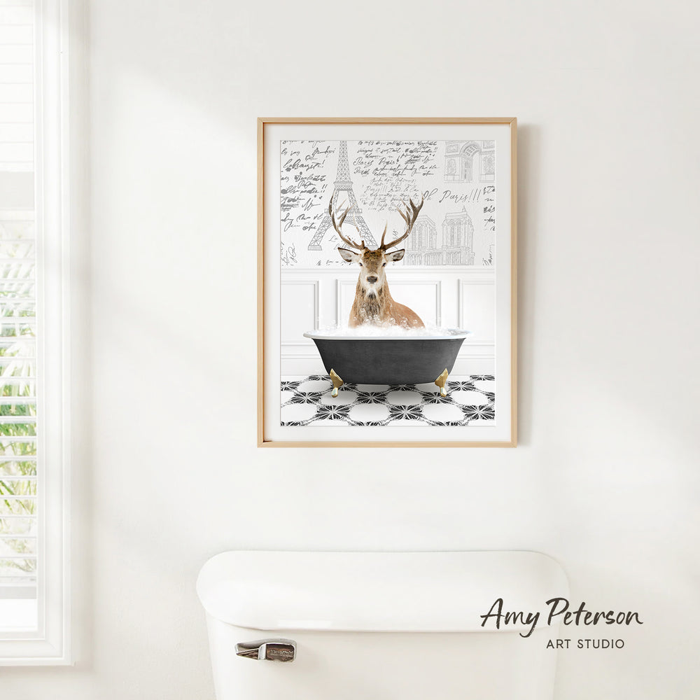 A framed print of a deer sitting in a bathtub is hanging on a white wall.