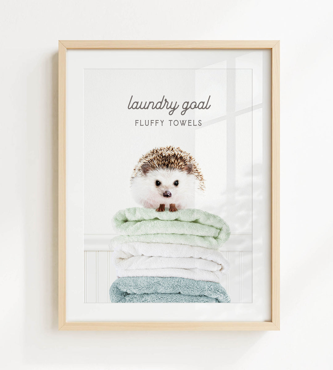 A framed image of a hedgehog sitting atop a stack of fluffy towels, with the text "laundry goal" and "fluffy towels" written above it.
