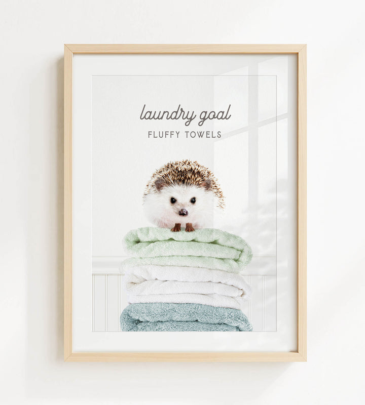 A framed image of a hedgehog sitting atop a stack of fluffy towels, with the text "laundry goal" and "fluffy towels" written above it.