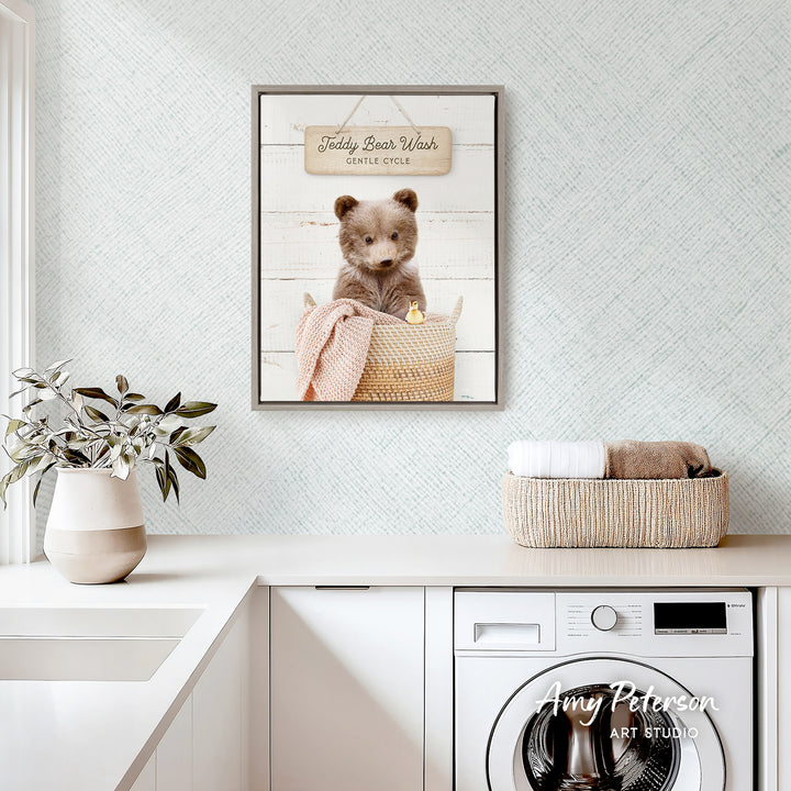a framed picture of a teddy bear sitting in a basket, placed on a white countertop in a kitchen setting.