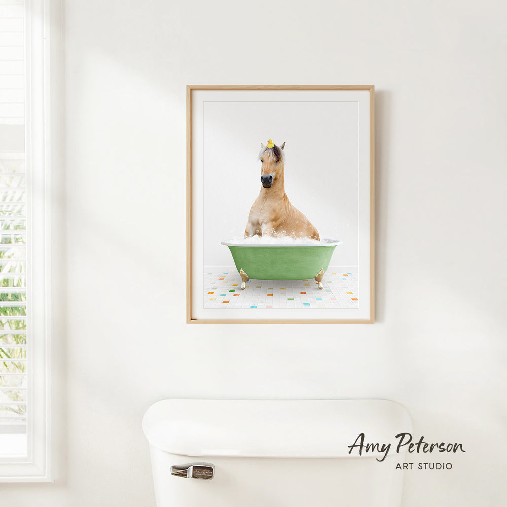 A framed image of a horse sitting in a green bathtub, with a yellow flower on its head, is hanging on a white wall.