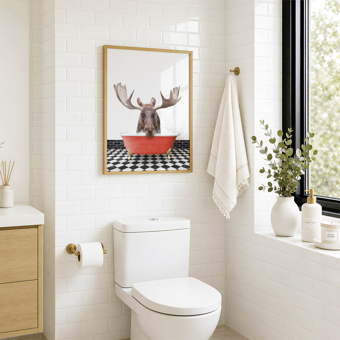 a bathroom with a white toilet, a framed picture of a moose in a red bathtub, and a towel hanging on a rack.