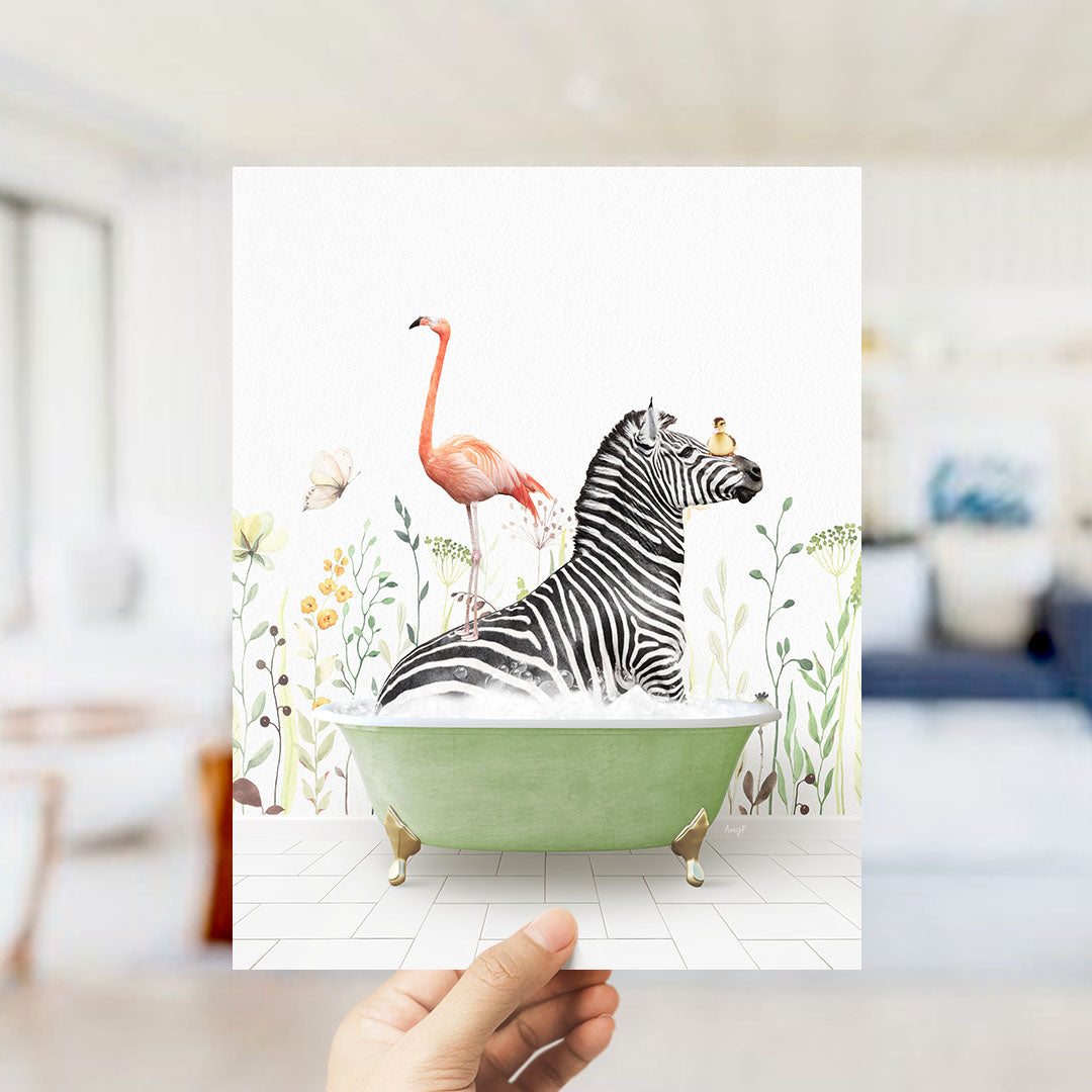 A hand holds up a framed image depicting a zebra sitting in a green bathtub, with a flamingo standing on its back and a bird perched on its head.