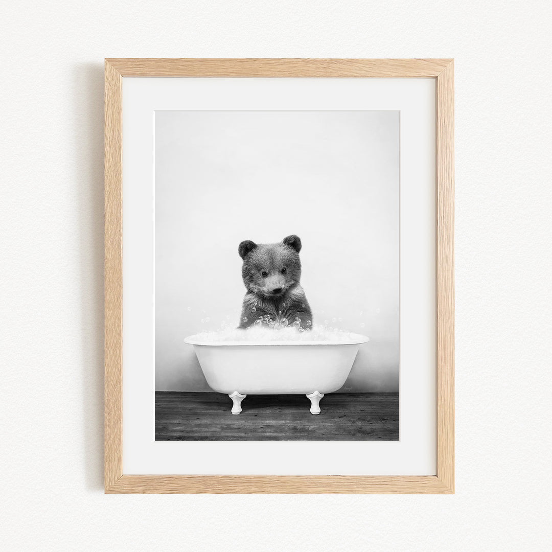 A black and white photograph of a bear sitting in a bathtub filled with water, creating a whimsical and playful scene.