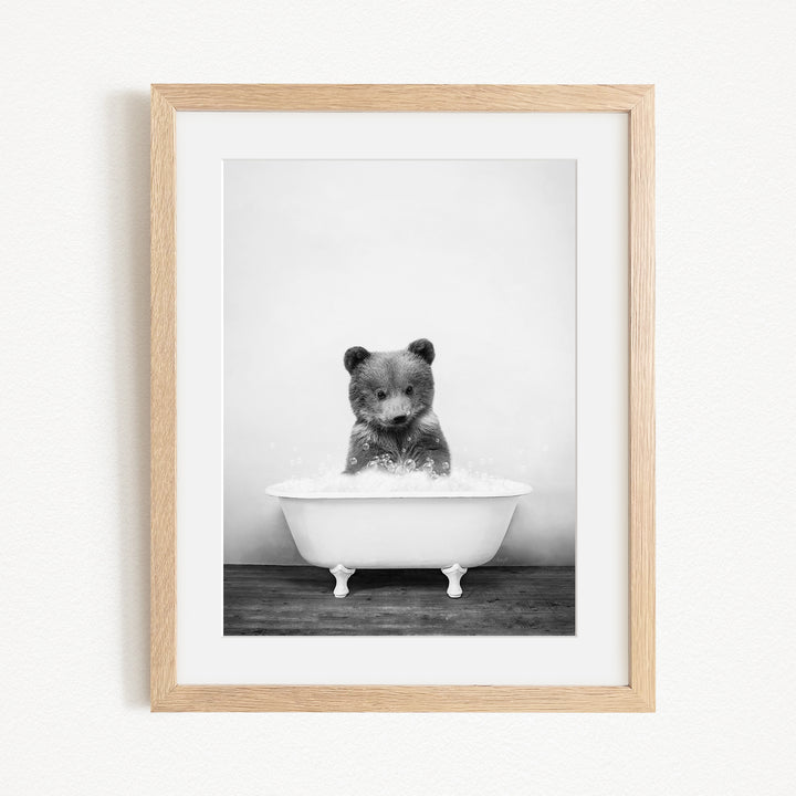 A black and white photograph of a bear sitting in a bathtub filled with water, creating a whimsical and playful scene.