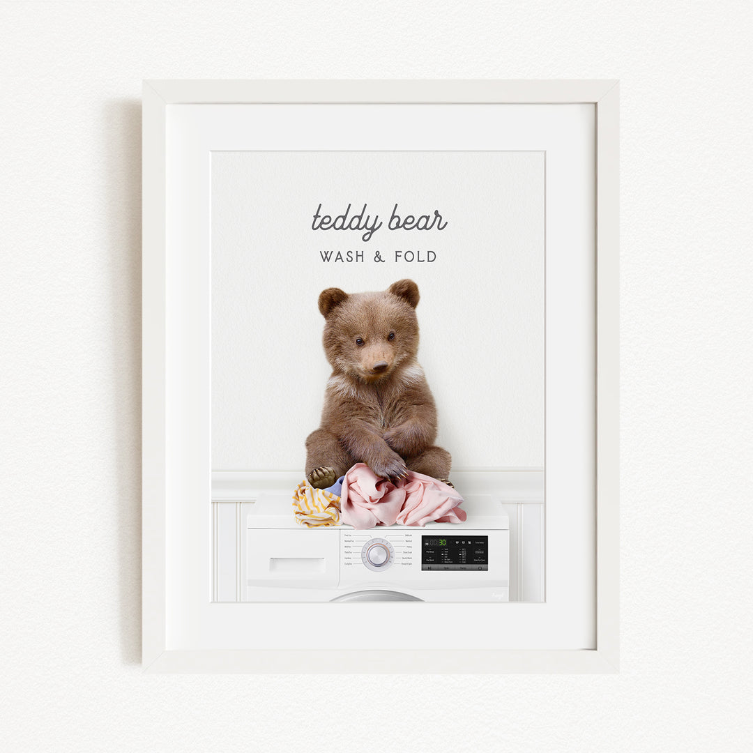 A teddy bear sitting on a washing machine, with the text "teddy bear" and "WASH & FOLD" written above it.