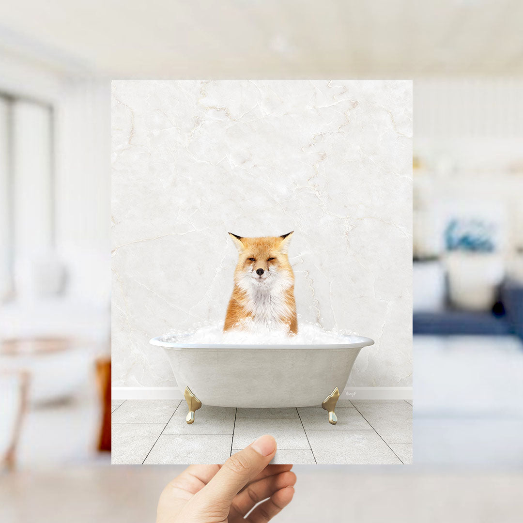 A hand holds up a framed image of a fox sitting in a bathtub filled with bubbles.