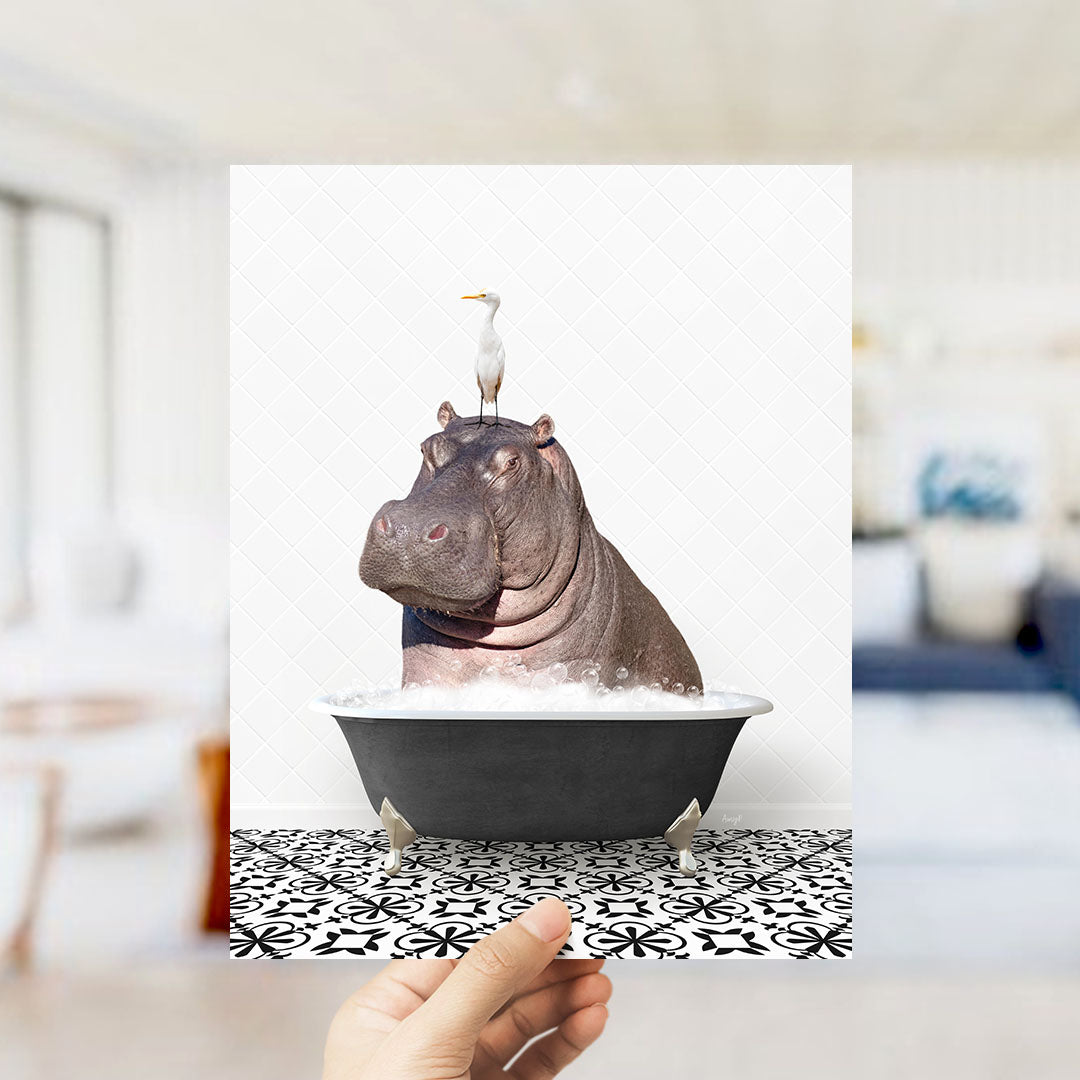 A hand holds up a framed image of a hippopotamus sitting in a bathtub, with a seagull perched on its head.