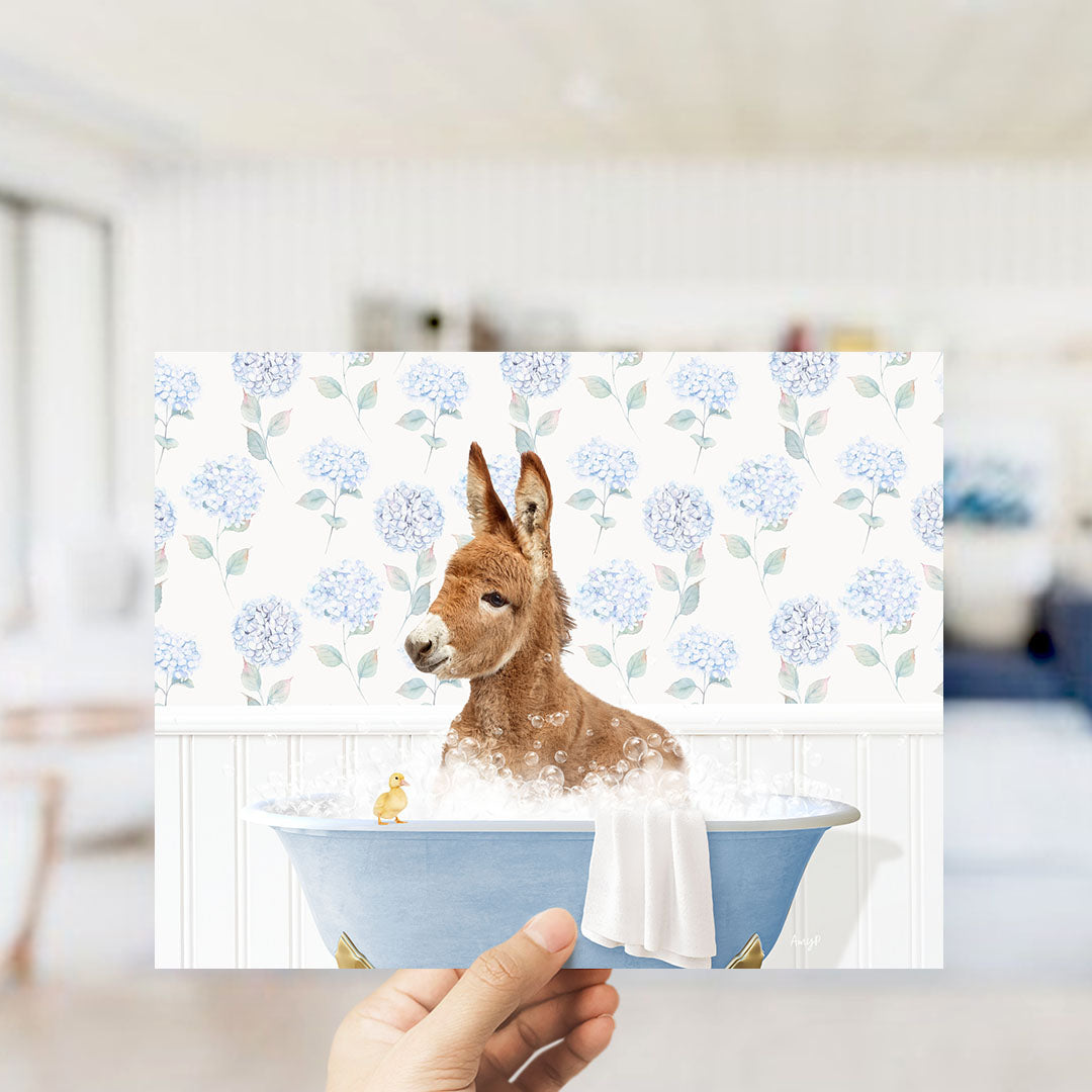 A hand holding a framed image of a brown dog sitting in a blue bathtub, surrounded by a floral pattern.