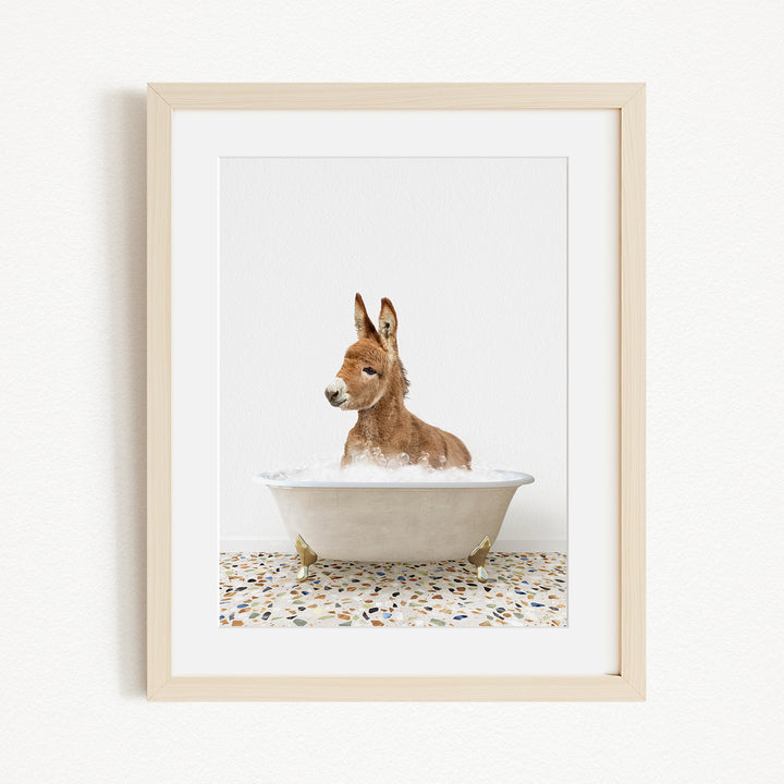 A donkey is sitting in a white bathtub filled with water, surrounded by a tiled floor.