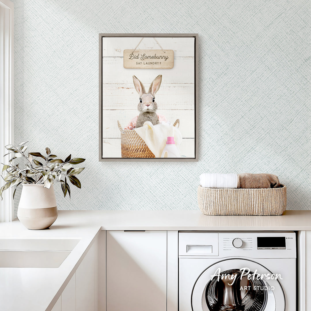 a laundry room with a framed picture of a rabbit sitting in a basket, a potted plant, and a basket of towels on a counter.