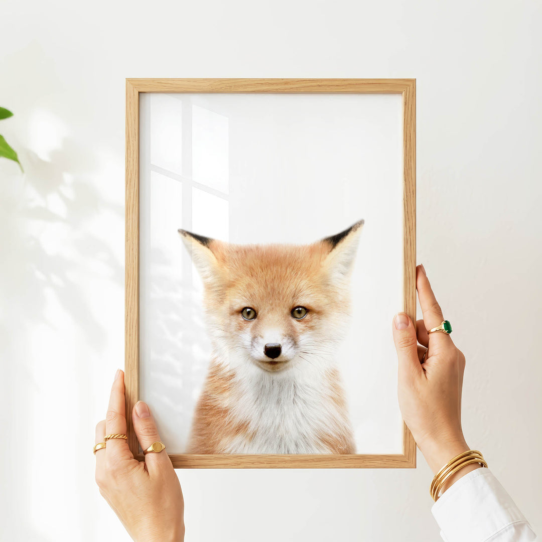 A person's hands are holding a wooden frame with a picture of a fox inside it.