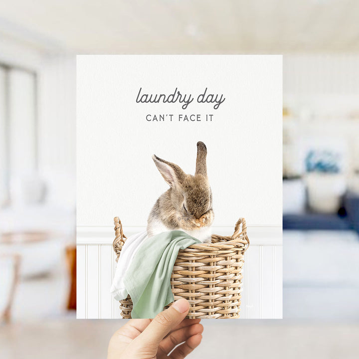 A hand holding a picture of a rabbit in a basket, with the text "laundry day can't face it" written above the image.