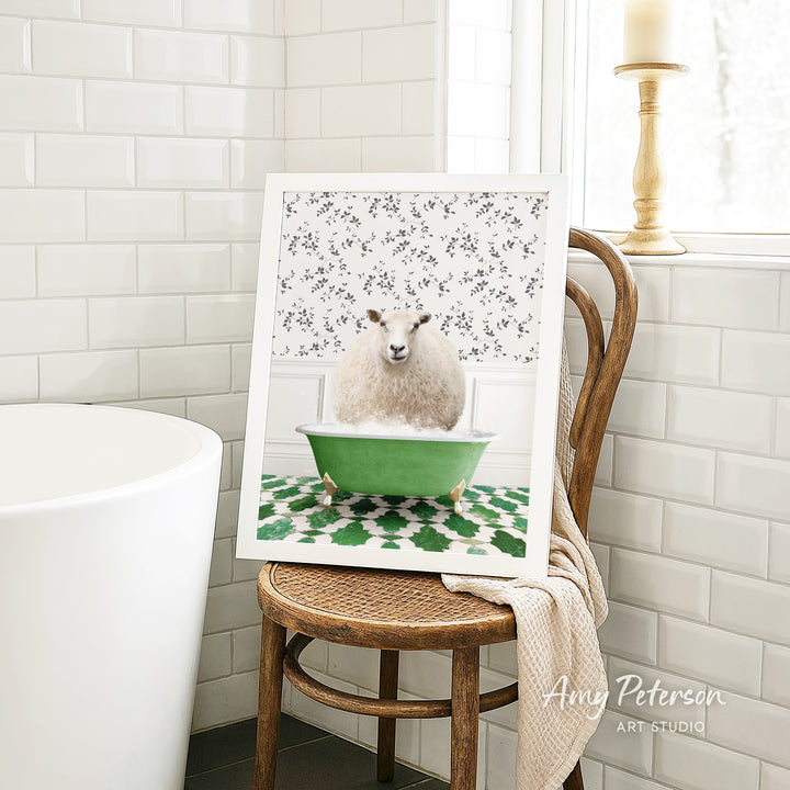 A framed image of a sheep sitting in a green bathtub, surrounded by a floral pattern, is displayed on a wooden chair in a bathroom setting.