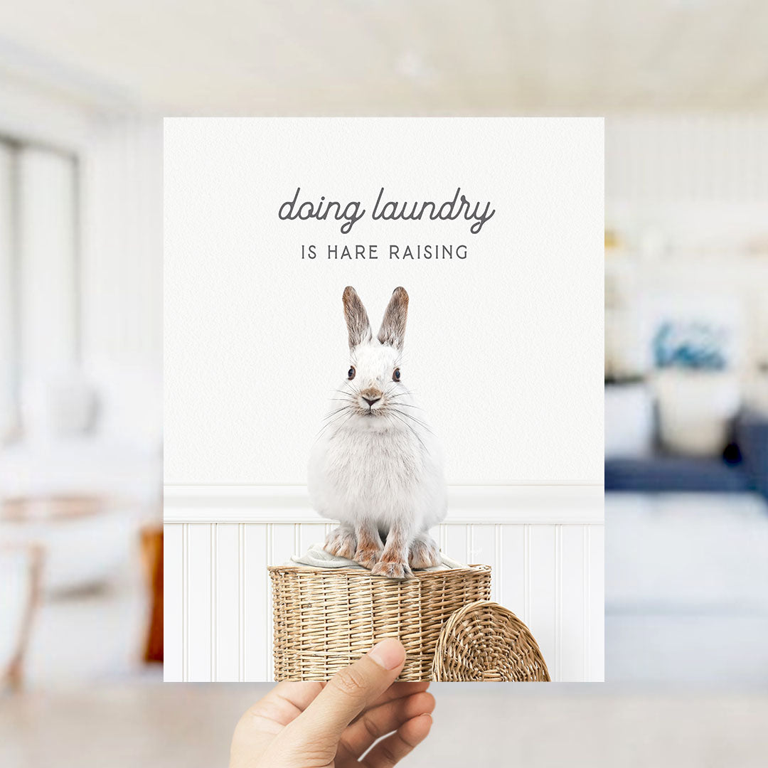 A white rabbit sitting on a woven basket, with the text "Doing laundry is Hare raising" displayed above the image.