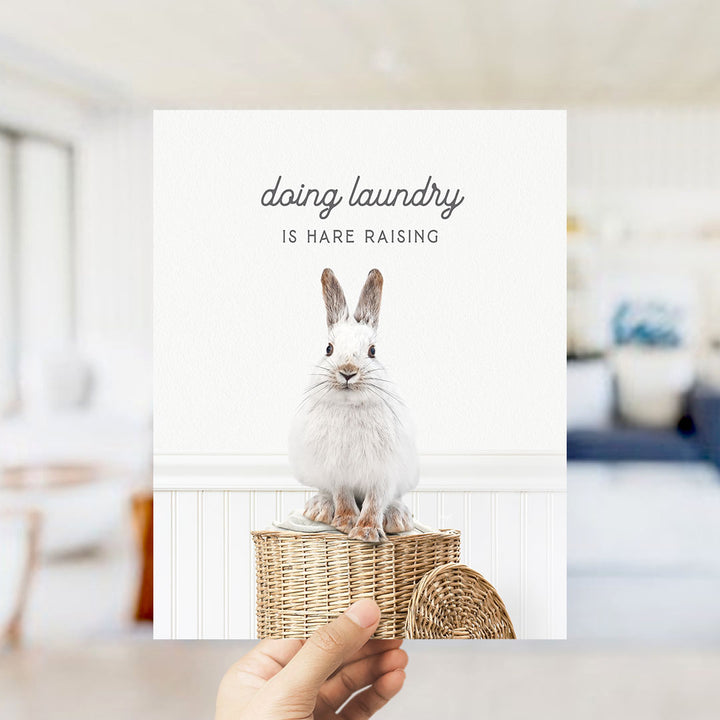 A white rabbit sitting on a woven basket, with the text "Doing laundry is Hare raising" displayed above the image.