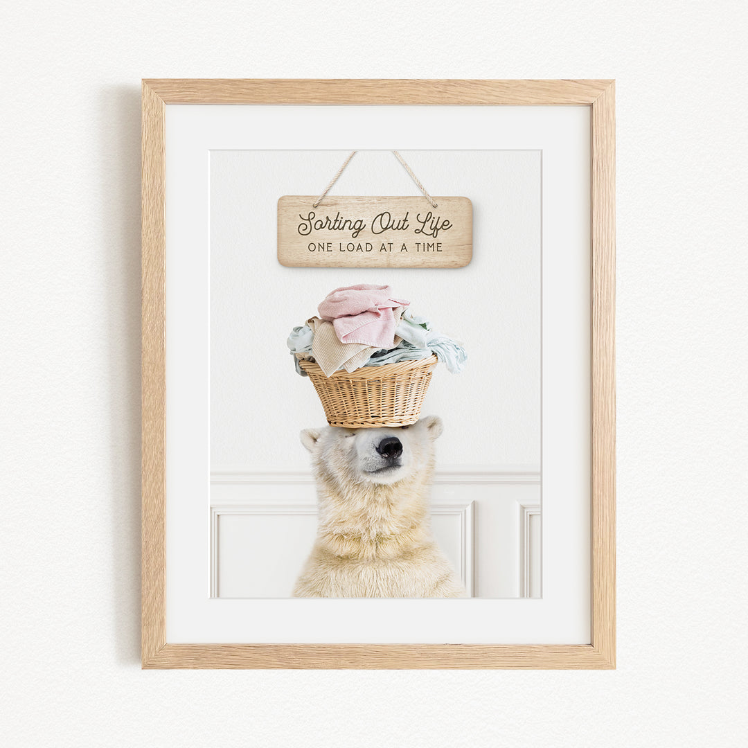 A polar bear balancing a basket of laundry on its head, with a sign above that reads "Sorting Out Life One Load at a Time".