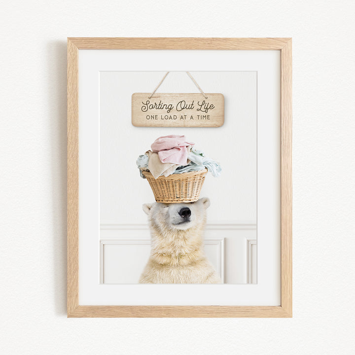 A polar bear balancing a basket of laundry on its head, with a sign above that reads "Sorting Out Life One Load at a Time".