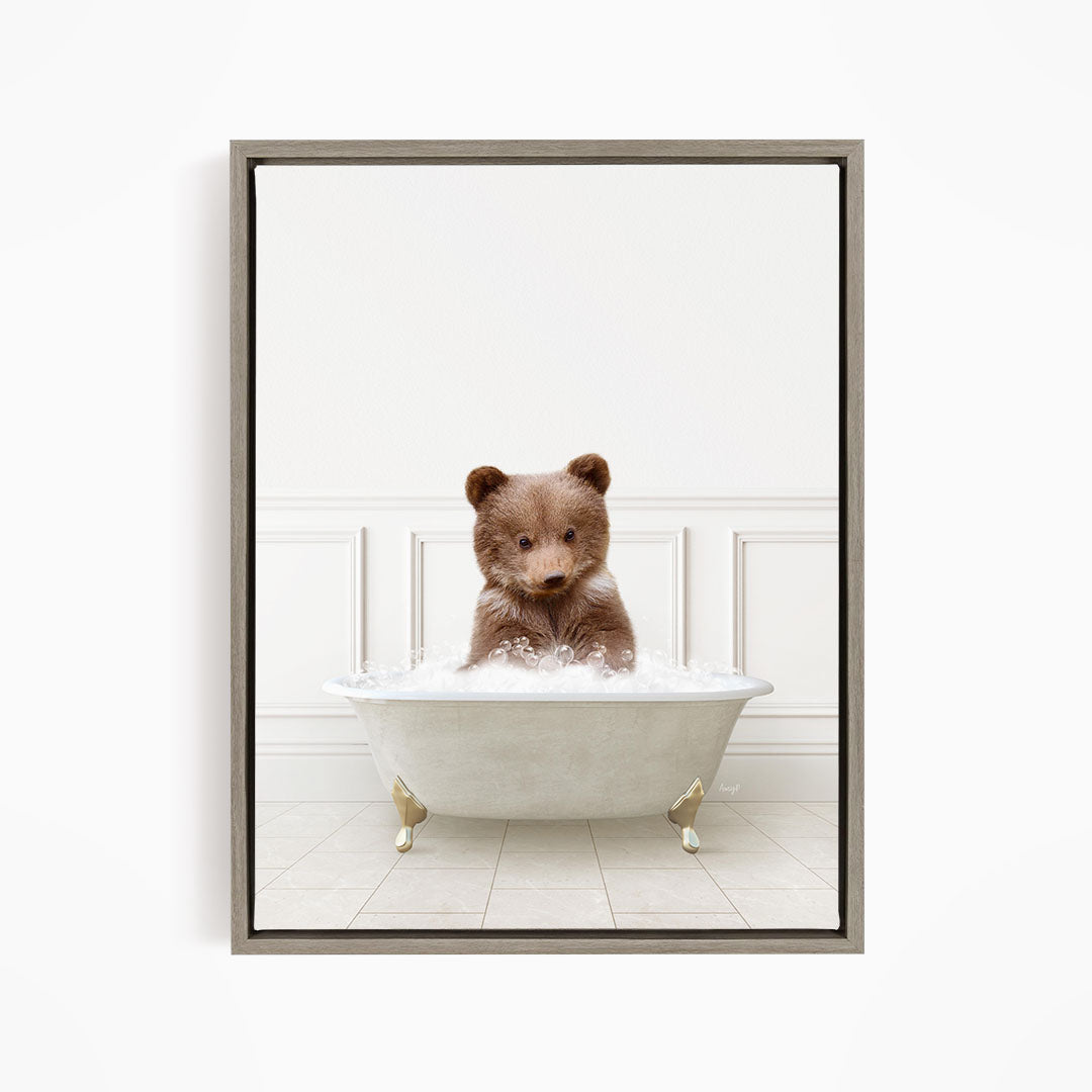 A cute brown bear sitting in a white bathtub filled with bubbles, looking directly at the camera.