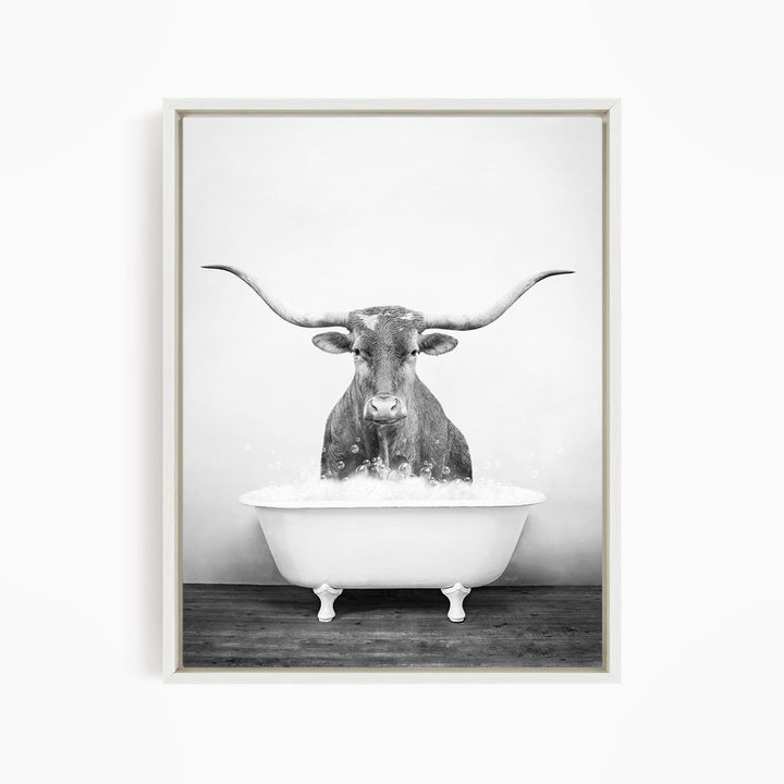 A black and white image of a bull with long horns sitting in a bathtub filled with water.