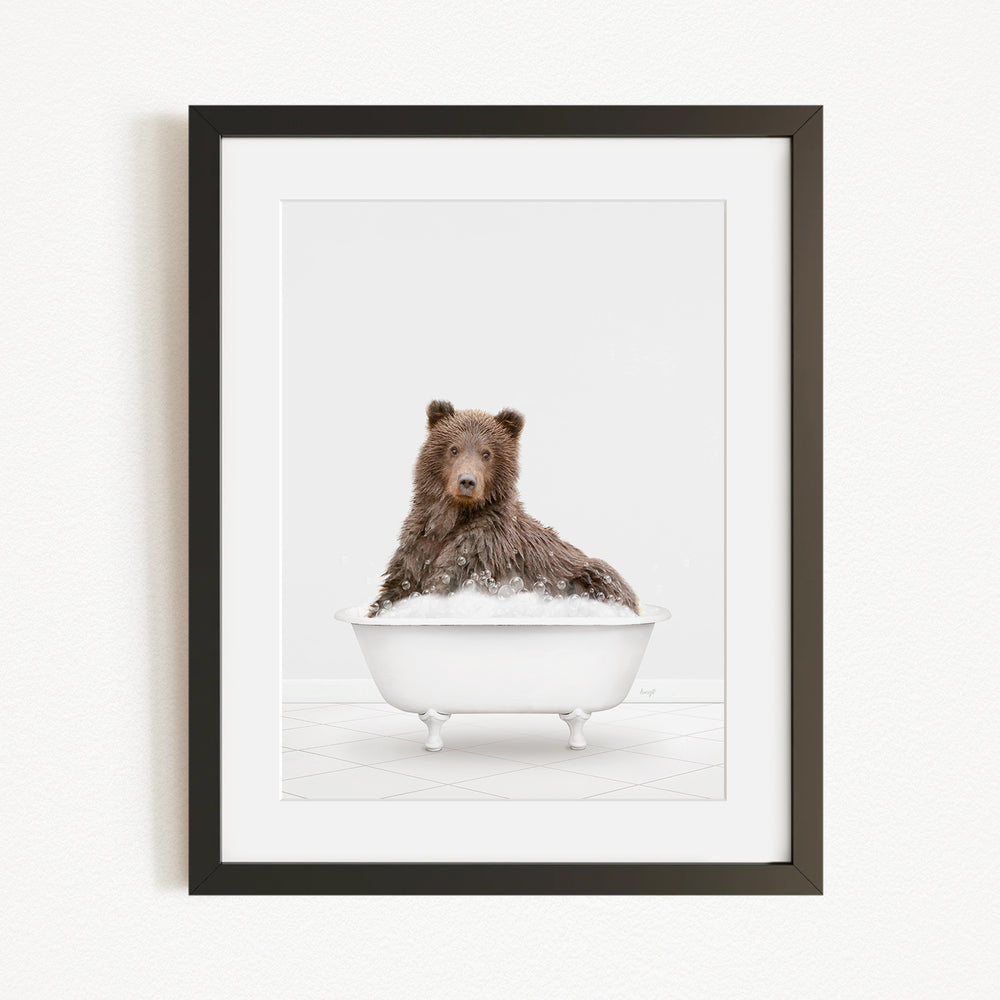 A brown bear sitting in a white bathtub filled with water, looking directly at the camera.