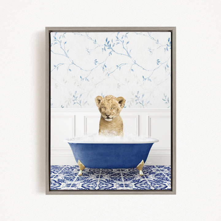 A young lion cub is sitting in a blue bathtub filled with water, surrounded by a blue and white patterned rug on the floor.