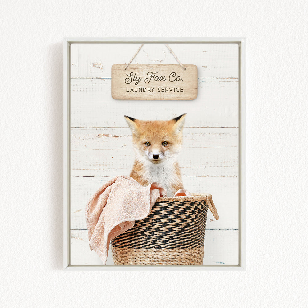 A framed image of a young fox sitting in a woven laundry basket, with a sign above it that reads "Slip Fox Co. Laundry Service".