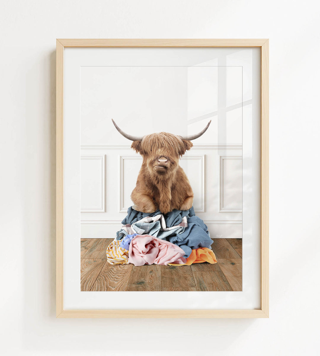 A brown cow with long horns is sitting on a pile of clothes on a wooden floor.