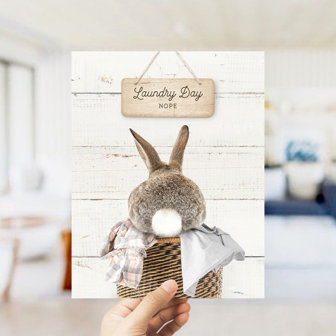 A wooden sign with the text "Laundry Day NOPE" hangs above a basket containing a rabbit.