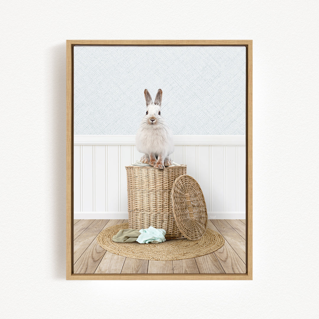 A white rabbit sits atop a woven basket on a wooden floor, with a green blanket and a basket lid nearby.