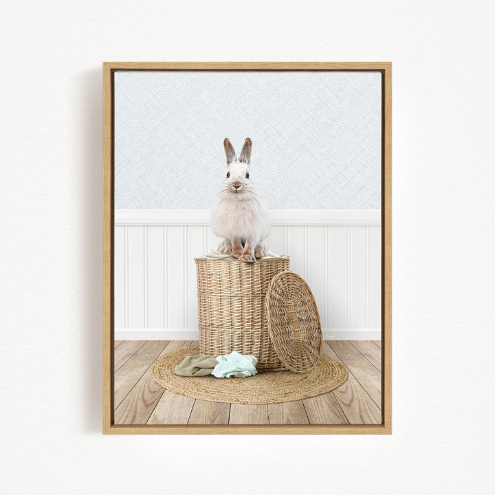 A white rabbit sits atop a woven basket on a wooden floor, with a green blanket and a basket lid nearby.