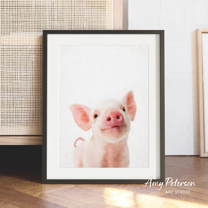 A framed photograph of a smiling pig is displayed on a wooden floor in front of a woven basket.