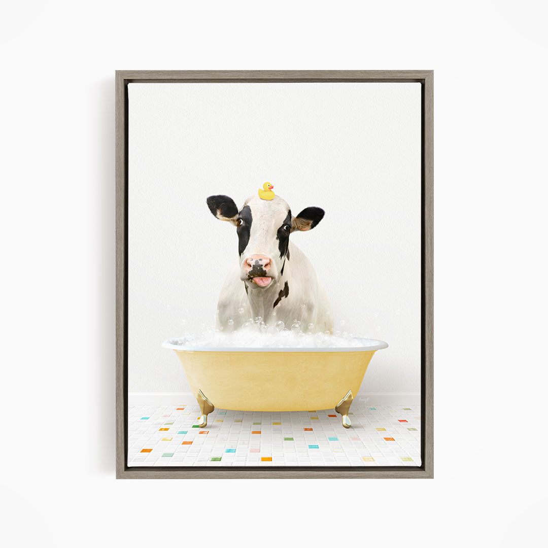 A black and white cow is sitting in a yellow bathtub filled with bubbles, with a rubber duck perched on its head.