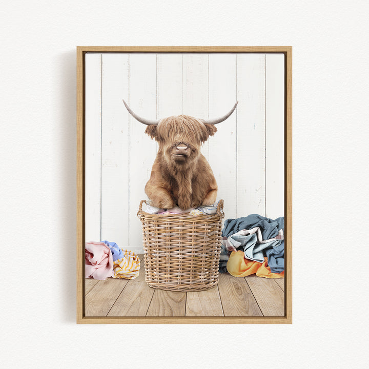 A Highland cow sits in a wicker basket filled with clothes, creating a whimsical and playful scene.