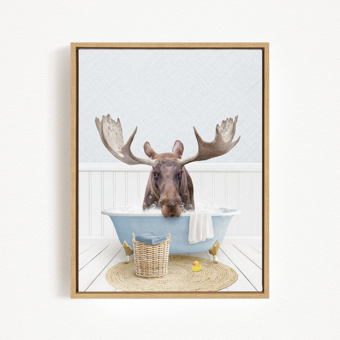 A moose is sitting in a bathtub filled with water, surrounded by a basket, a yellow rubber duck, and a towel.