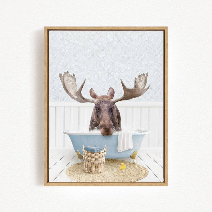 A moose is sitting in a bathtub filled with water, surrounded by a basket, a yellow rubber duck, and a towel.