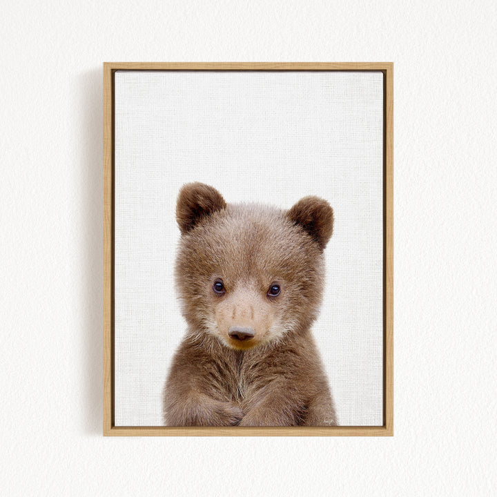 A young brown bear cub with large, expressive eyes and a curious expression is the focal point of the framed image.