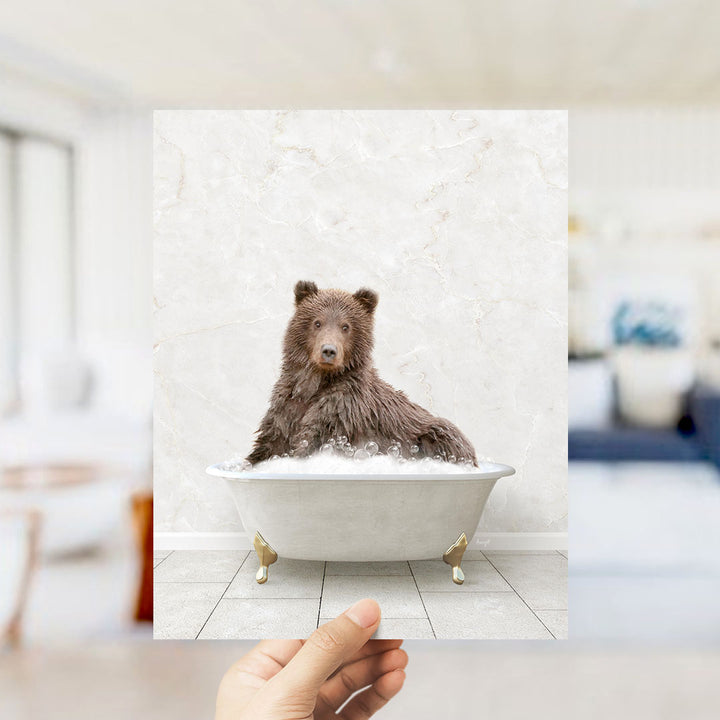 A brown bear sitting in a white bathtub filled with bubbles, with a blurred background suggesting a bathroom setting.