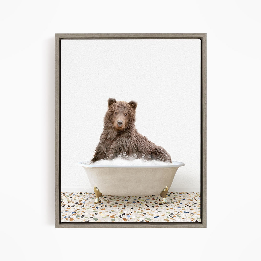 A brown bear sitting in a white bathtub filled with bubbles, looking directly at the camera.