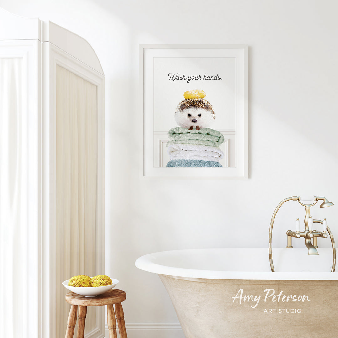 a bathroom with a framed poster of a hedgehog on a towel, a wooden stool with a bowl of fruit, and a clawfoot bathtub with a faucet.