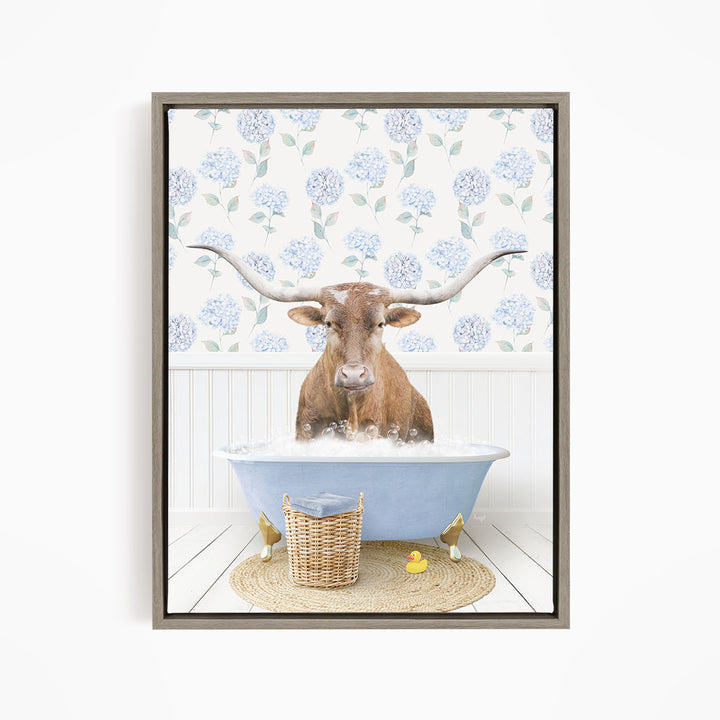 A brown steer with large horns is sitting in a blue bathtub filled with water, surrounded by a wicker basket and yellow rubber ducks.
