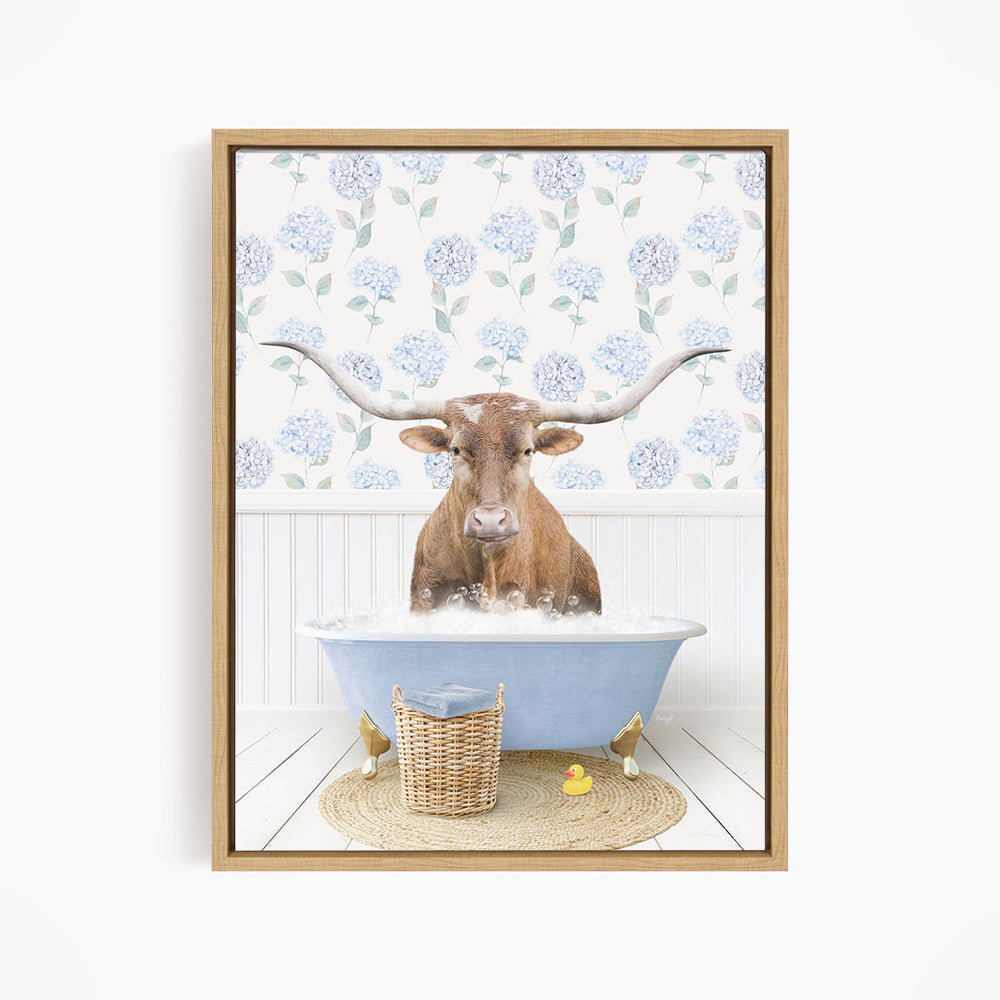 A brown steer with large horns is sitting in a blue bathtub filled with water, surrounded by a wicker basket and rubber ducks.