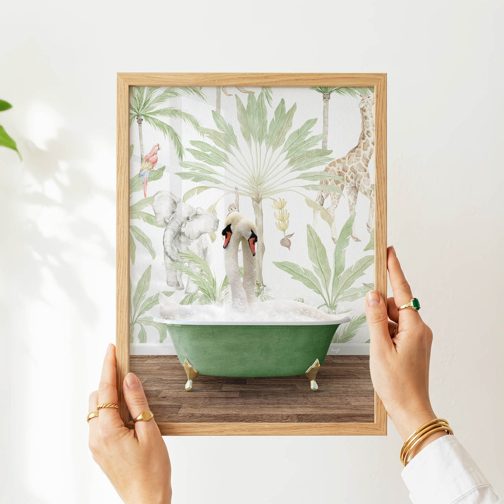 A person's hands are holding a framed picture of a green bathtub with two swans sitting in it, surrounded by tropical foliage.