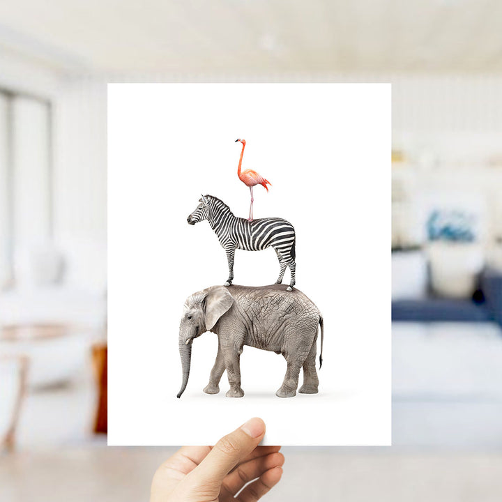 A hand is holding up a white card with a picture of a zebra, a flamingo, and an elephant standing on top of it.