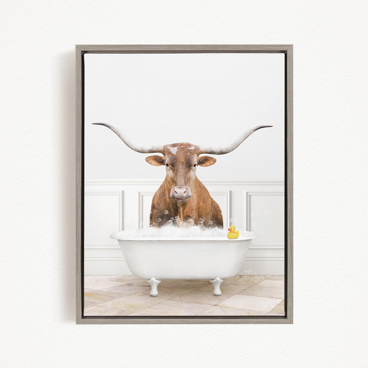 A brown bull with long horns is sitting in a white bathtub filled with bubbles, with a yellow rubber duck floating in the water.