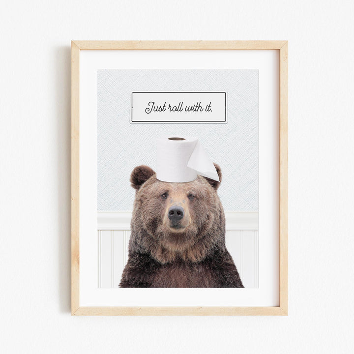 A framed image of a brown bear wearing a toilet paper hat, with the text "Just roll with it."